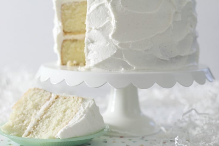 favorite vanilla bean cake on white cake stand with slice cut on a small green plate